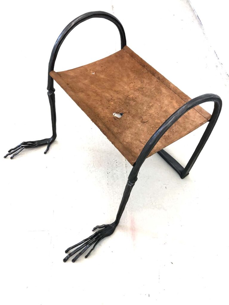 A sculpture of a steel stool that has human hands, and a leather seat.