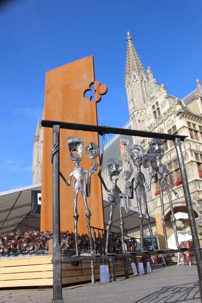 A steel sculpture of four disfigured people holding masks to cover over missing facial features.