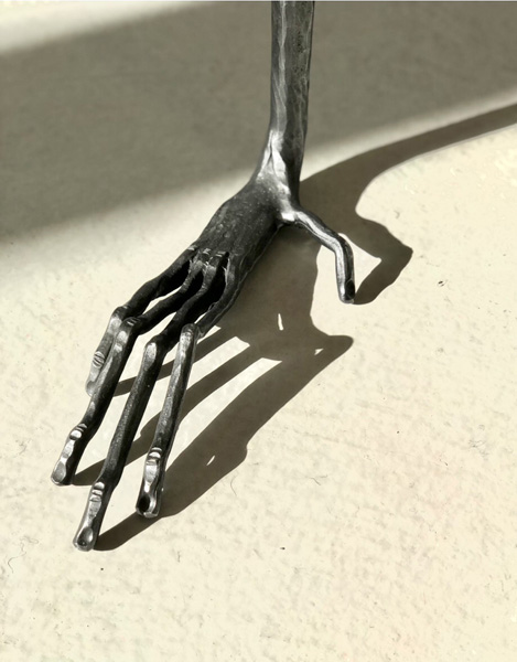 A forged steel hand with long spindly fingers and strong shadows.