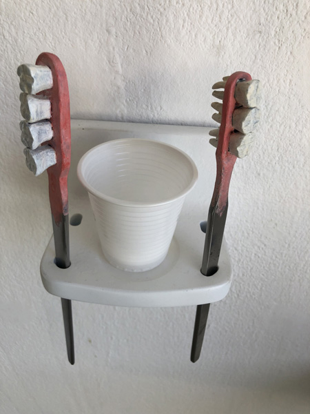 Two toothbrushes with teeth instead of bristles, in a toothbrush holder and a plastic cup